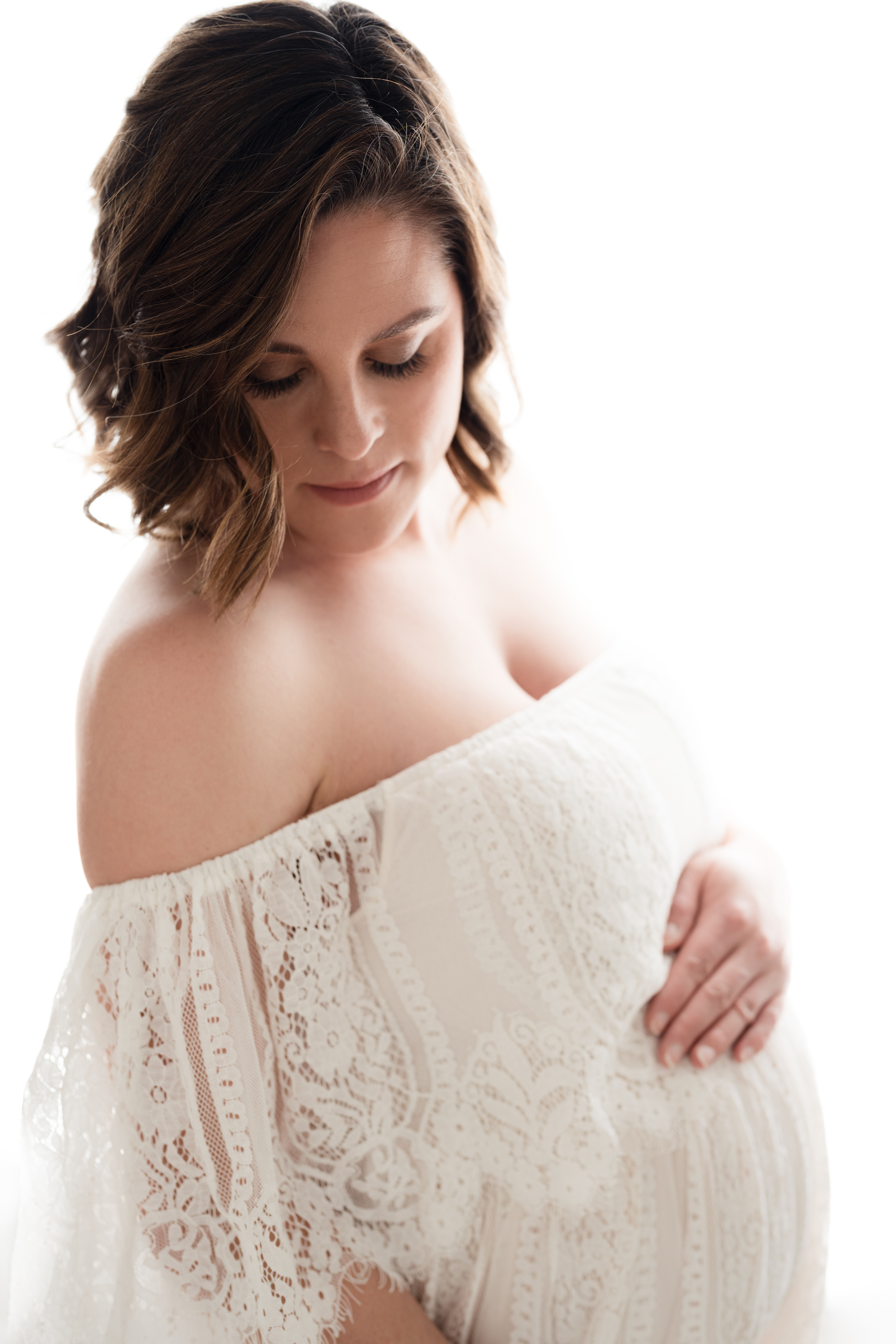 Fine art studio maternity portrait of a pregnant woman lit from behind, reflecting when to book maternity photos for elegant, natural light images