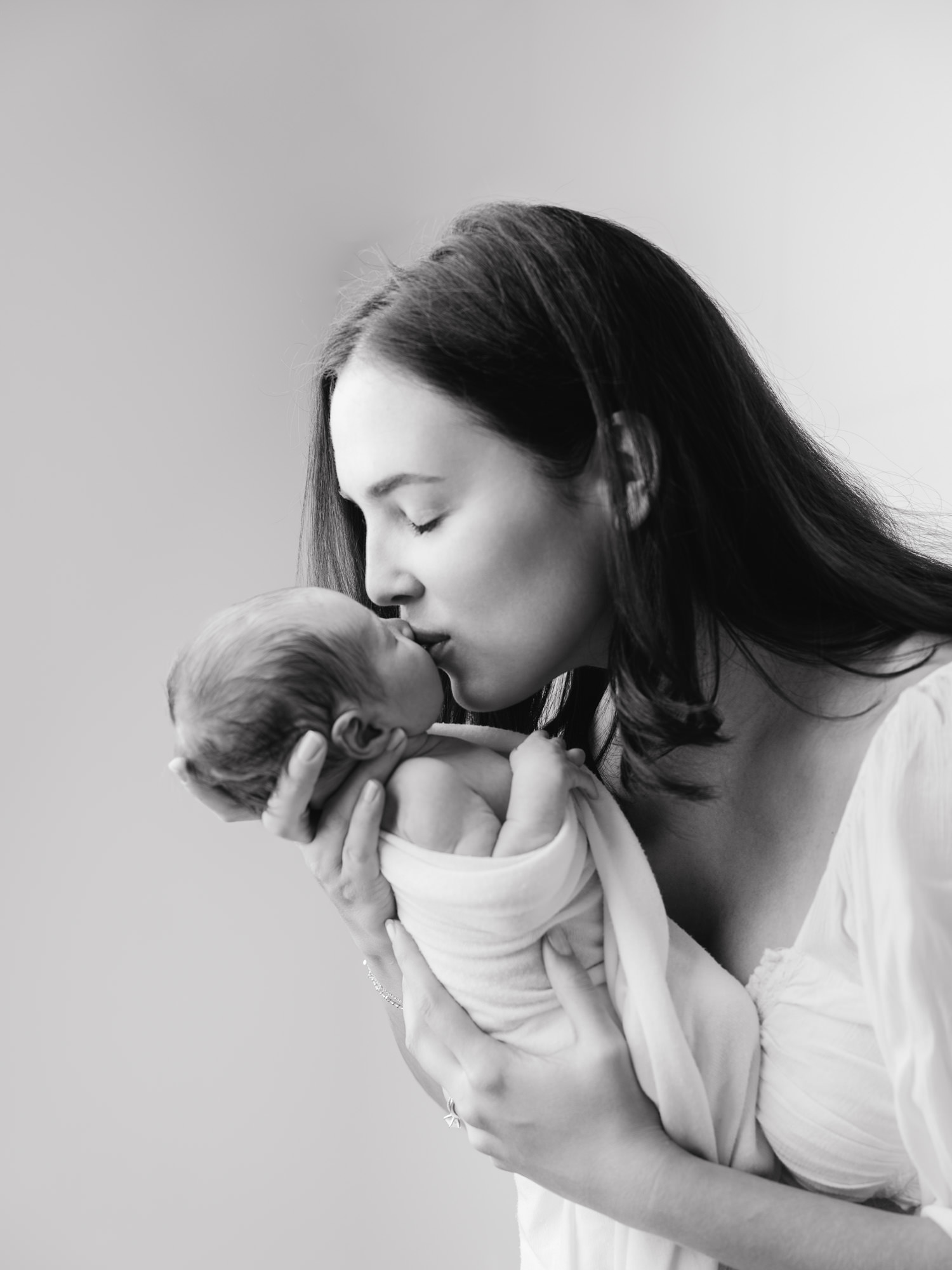 Mother gently kissing her newborn baby boy during lifestyle session in Roseville studio