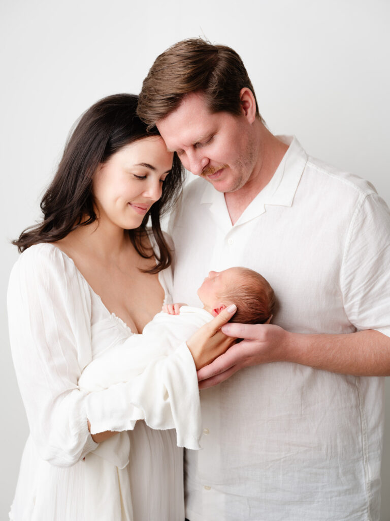 New parents lovingly cradling their newborn baby in a serene studio setting, showcasing the warmth and intimacy of family photography by Sweet Jean Photography.