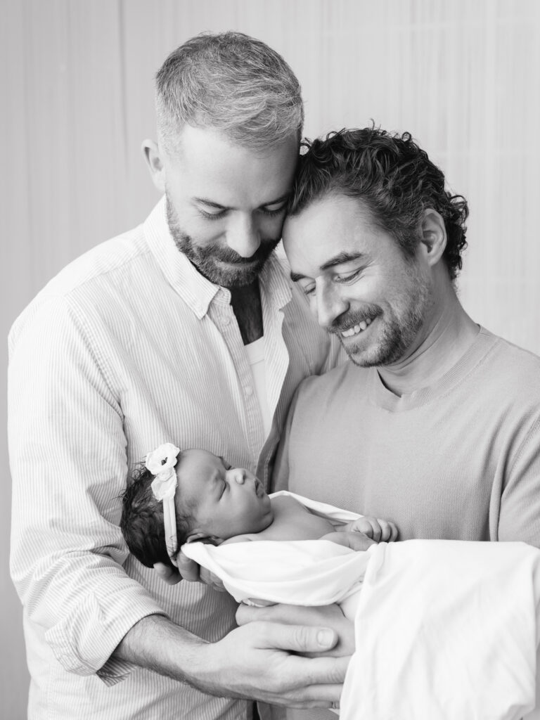 Two fathers holding their newborn in a family photography session in a Sacramento studio