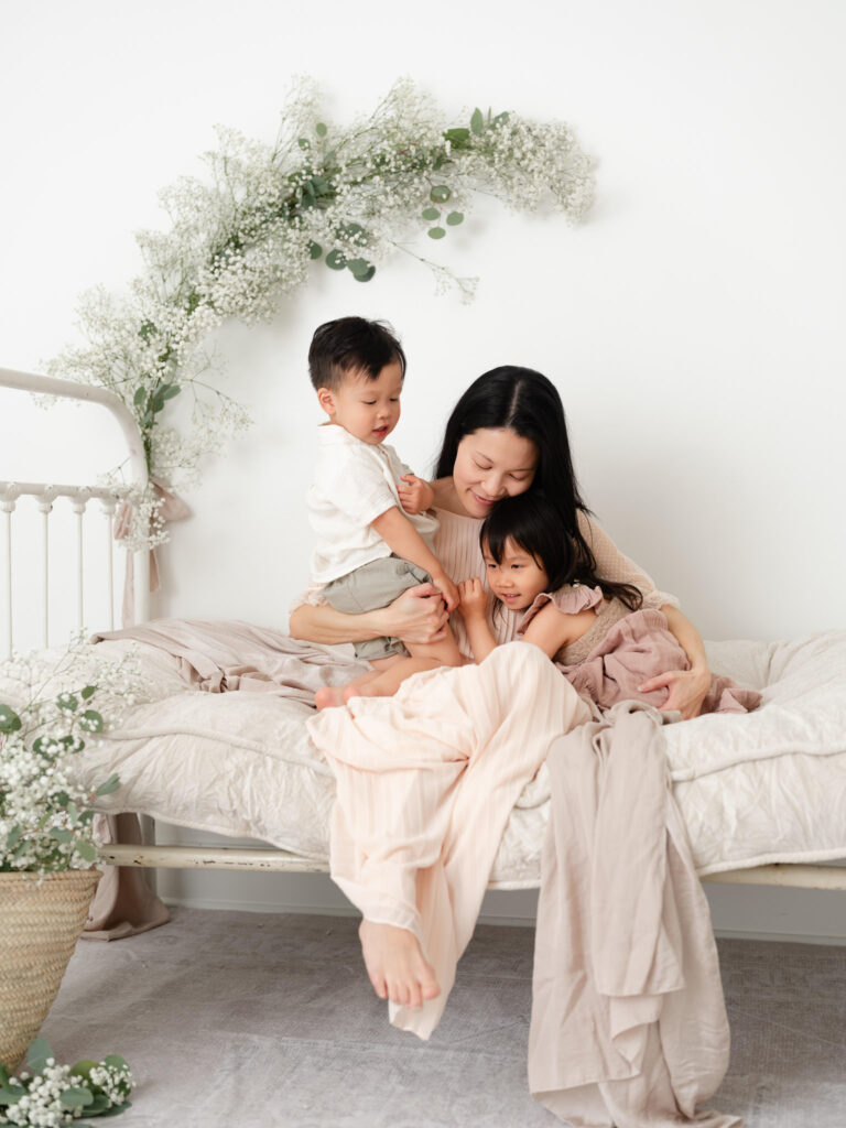 Sacramento Motherhood Photography Event Mother snuggling with children on a vintage daybed surrounded by florals