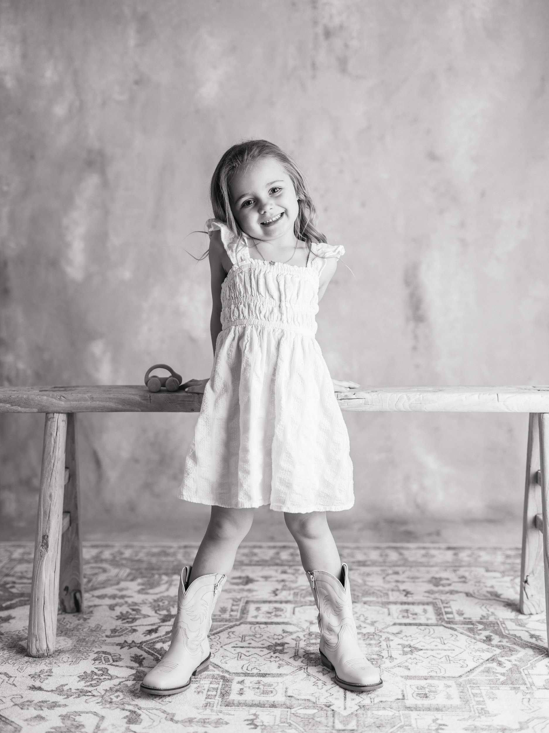 Fine art black and white studio portrait of a young girl standing confidently in a white dress, photographed for The Light Between childhood series.