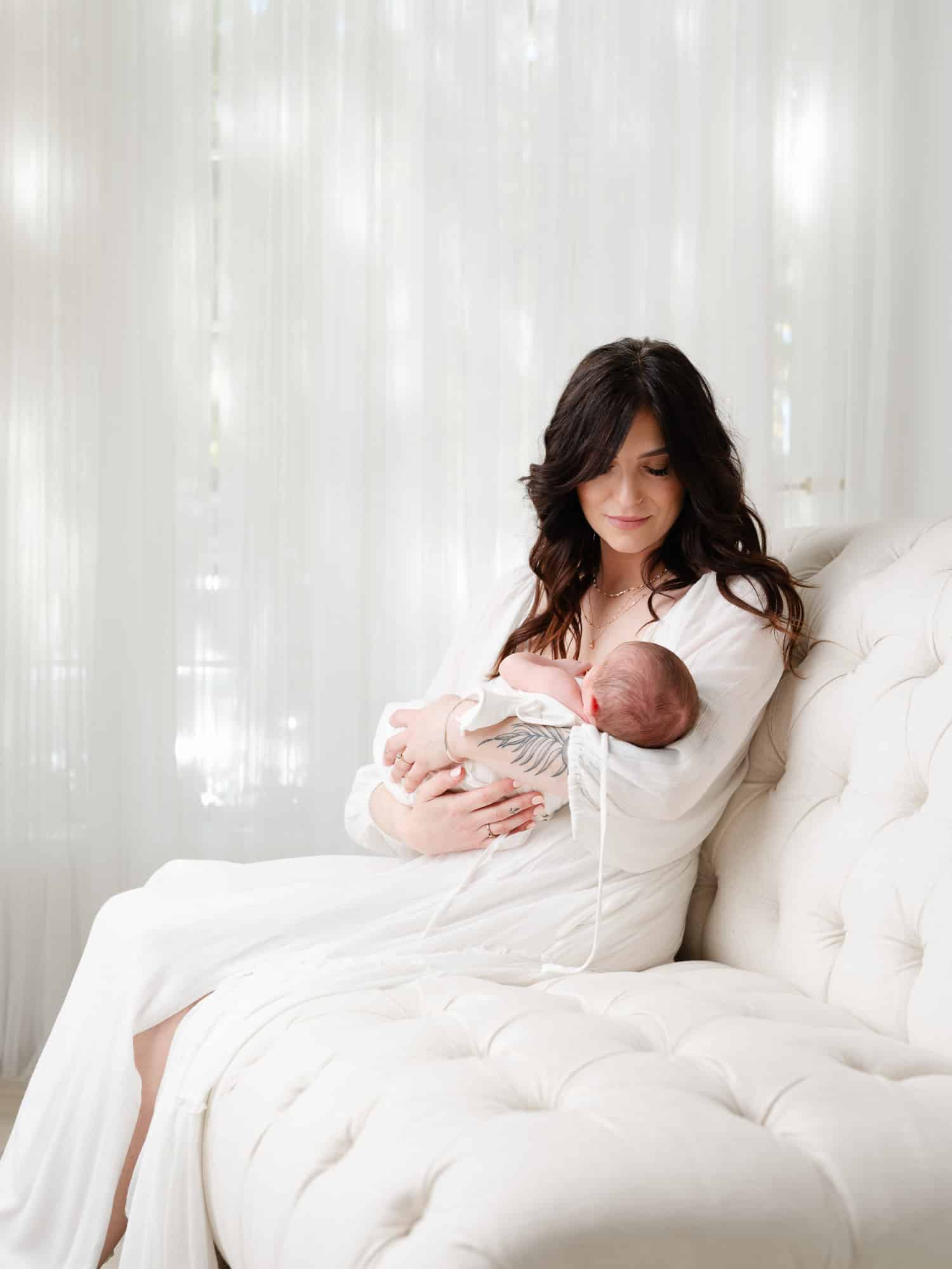 Mother holding newborn baby boy wearing a flowing cream gown with professional hair and makeup, Sacramento studio